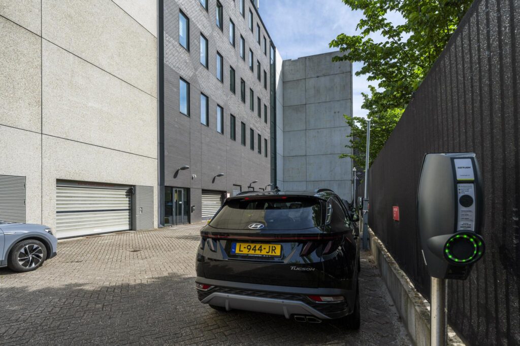 Electric car charging next to a modern office building on Krijn Taconiskade.